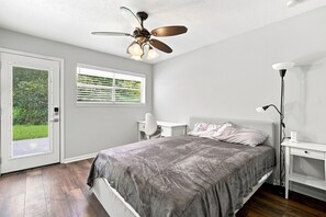 Ein Schlafzimmer mit einem Bett, einem Deckenventilator, einem Fenster mit Jalousien und einem Nachttisch mit Lampe.