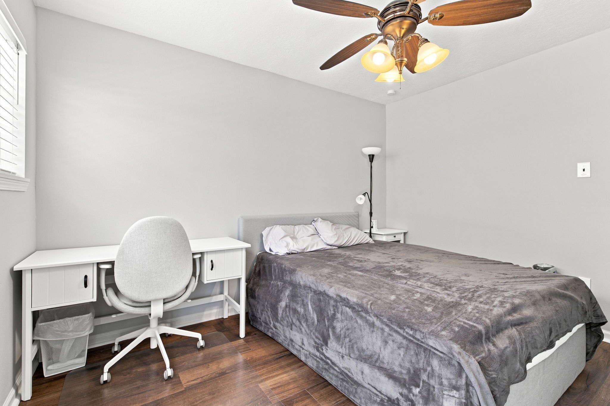 A bedroom with a bed, desk, chair, and a ceiling fan.