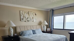 Ein Schlafzimmer mit einem Bett, zwei Nachttischen, einem Kunstwerk an der Wand, einem Fenster mit Blick und einem Schild auf dem Nachttisch.