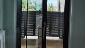 Une salle de bain dotée d’une porte en verre donnant sur un balcon avec vue sur l’océan et les palmiers.