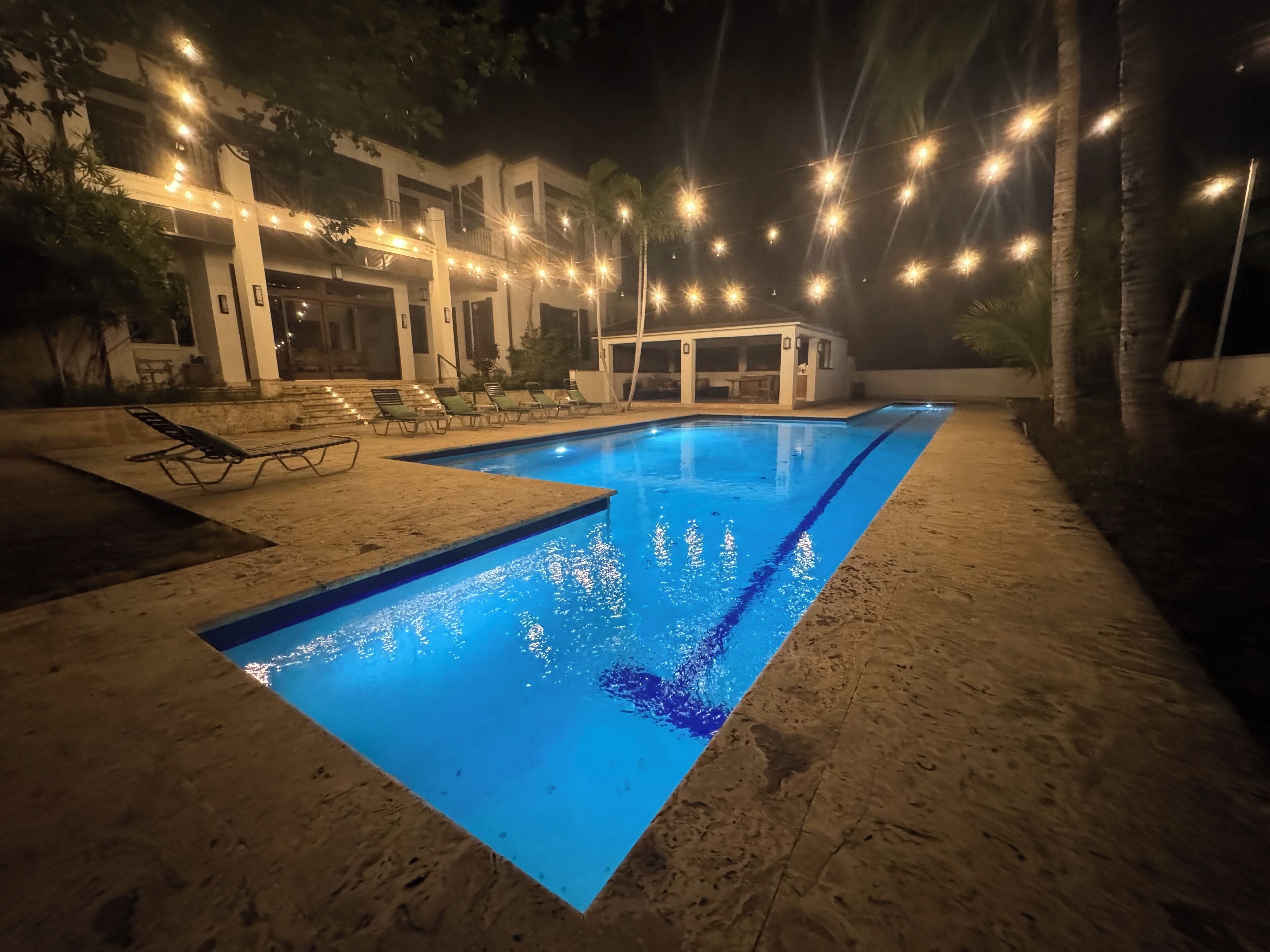 A swimming pool with a clear blue waterline, surrounded by lounge chairs and a covered seating area.