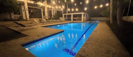 A swimming pool with a clear blue waterline, surrounded by lounge chairs and a covered seating area.