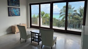 Une pièce spacieuse avec un grand balcon, deux fauteuils, une petite table et des œuvres d’art accrochées au mur.