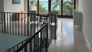 Un balcon spacieux offrant une vue sur l’océan, un coin repas agrémenté d’une rambarde et des œuvres d’art accrochées au mur.