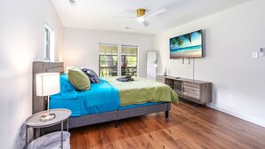 Un dormitorio moderno con cama, escritorio, televisión y vistas al balcón.