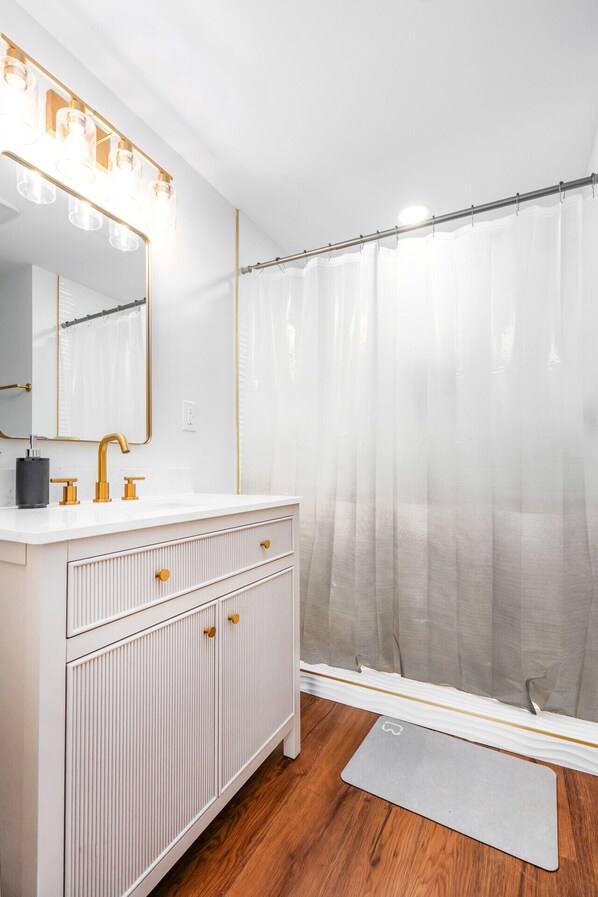 A bathroom with a white vanity, gold fixtures, and a shower curtain with a leaf pattern. - 2 Fishing Ponds, 5 Acres of Privacy | Remodeled Hideaway (Somerville)