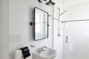 A modern bathroom with a white sink, a large mirror, and a glass-enclosed shower.
