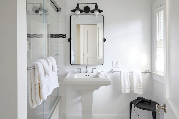 Ein modernes Badezimmer mit einem weißen Waschbecken, einem großen Spiegel und einer Duschkabine aus Glas.