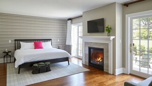 A bedroom with a bed, a fireplace, a TV, and a view of the outdoors. - The Kent Collection - The Firefly Inn (Kent)