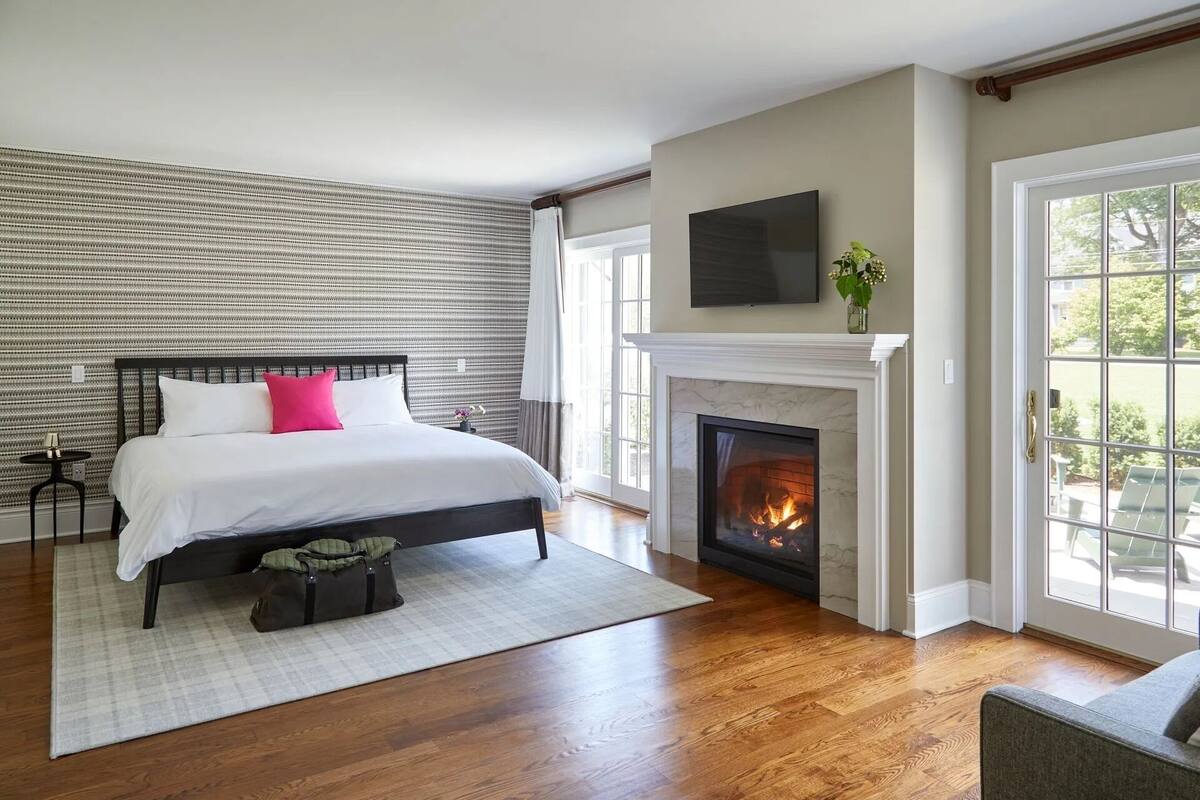 A bedroom with a bed, a fireplace, a TV, and a view of the outdoors.