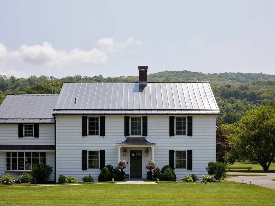 A two-story white house with a metal roof, a front porch, and a well-maintained lawn.
