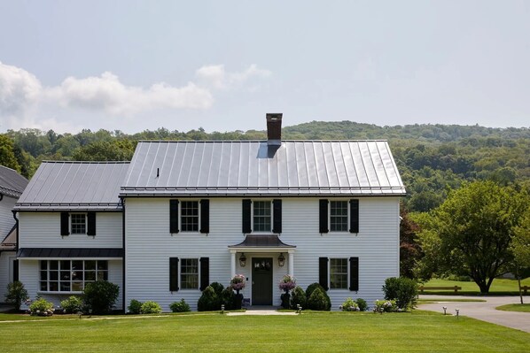 A two-story white house with a metal roof, a front porch, and a well-maintained lawn.