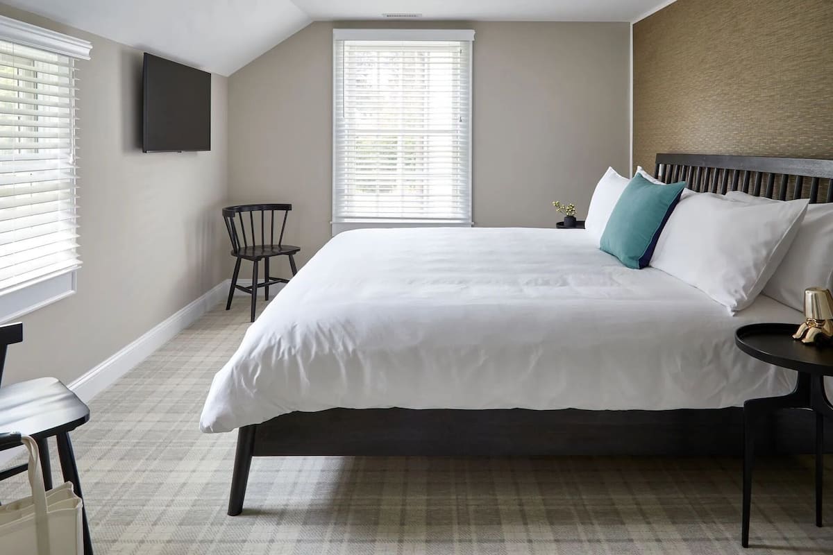 A bedroom with a large bed, a chair, a small table, and a TV mounted on the wall.