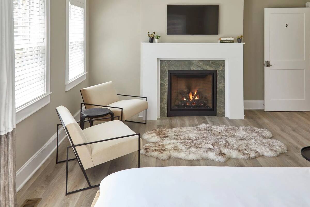 A modern bedroom with a fireplace, a sofa, a chair, and a fur rug.