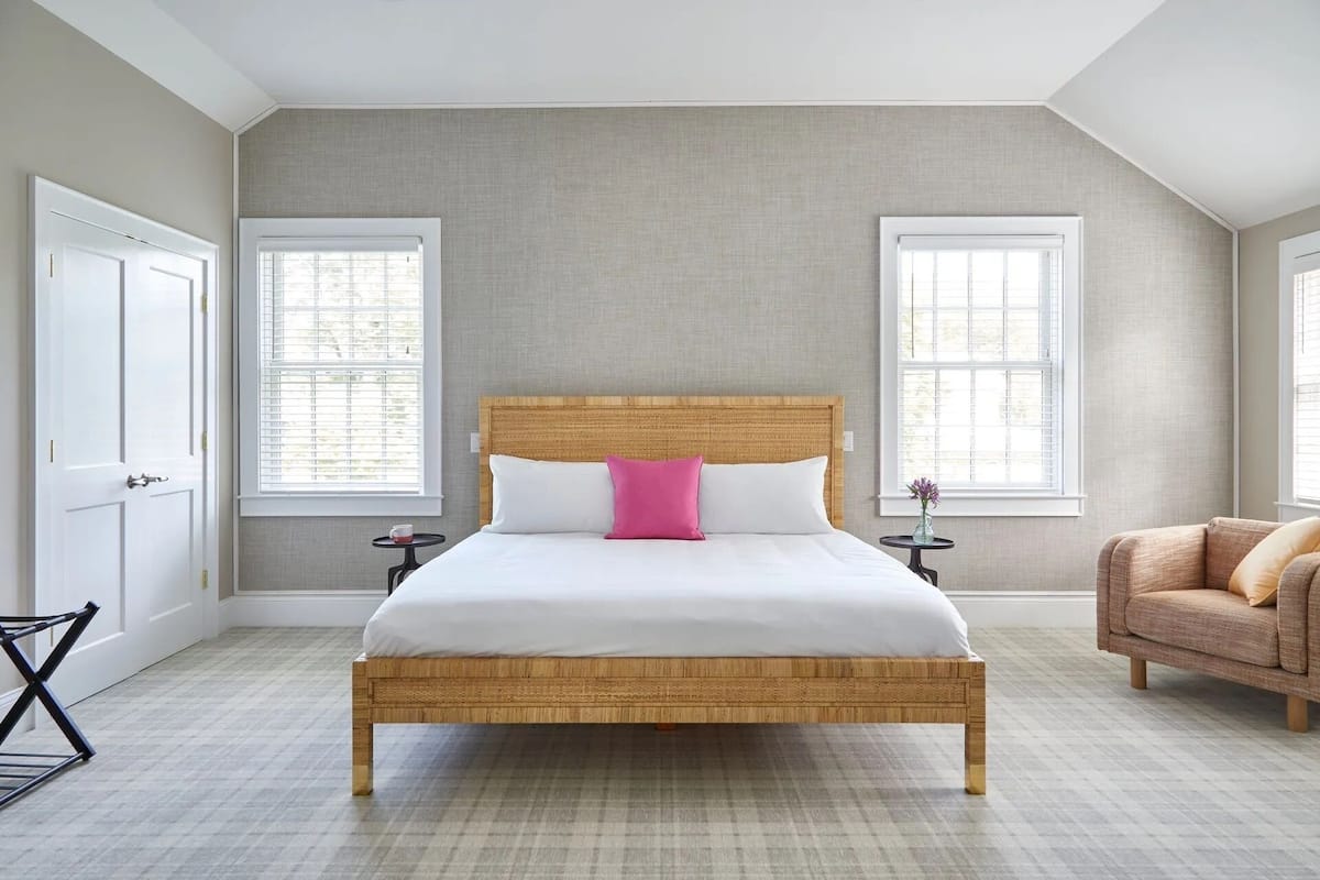 A bedroom with a large bed, two bedside tables, a chair, and a window with blinds.