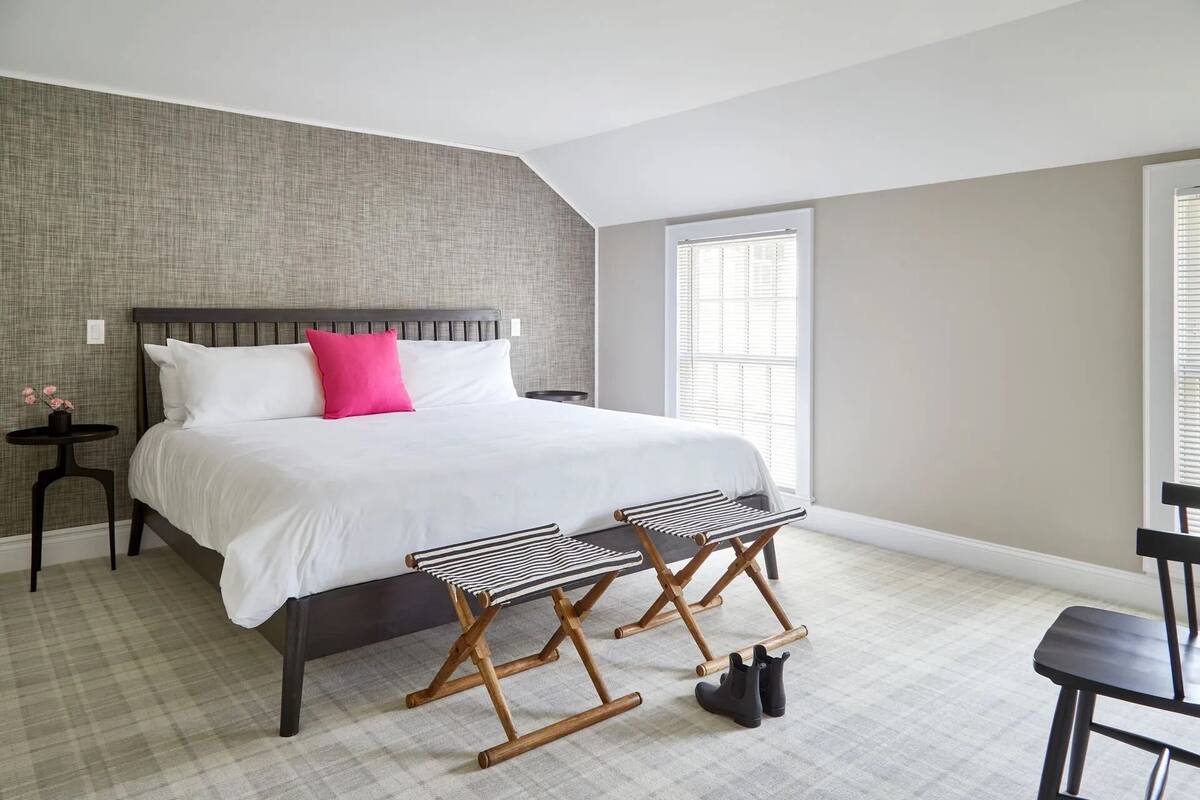 A bedroom with a large bed, a nightstand, a window, and a chair.