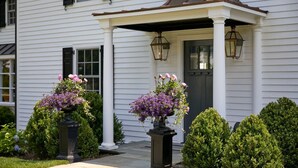 A white house with a porch, two flower planters, and a well-maintained lawn. - The Kent Collection - The Firefly Inn (Kent)