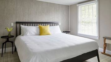 Um quarto com uma cama grande, uma mesa de cabeceira, uma pequena mesa com um vaso, e uma janela com persianas.