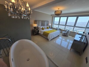 A modern hotel room with a large bed, a bathtub, a desk, and a view of the city.