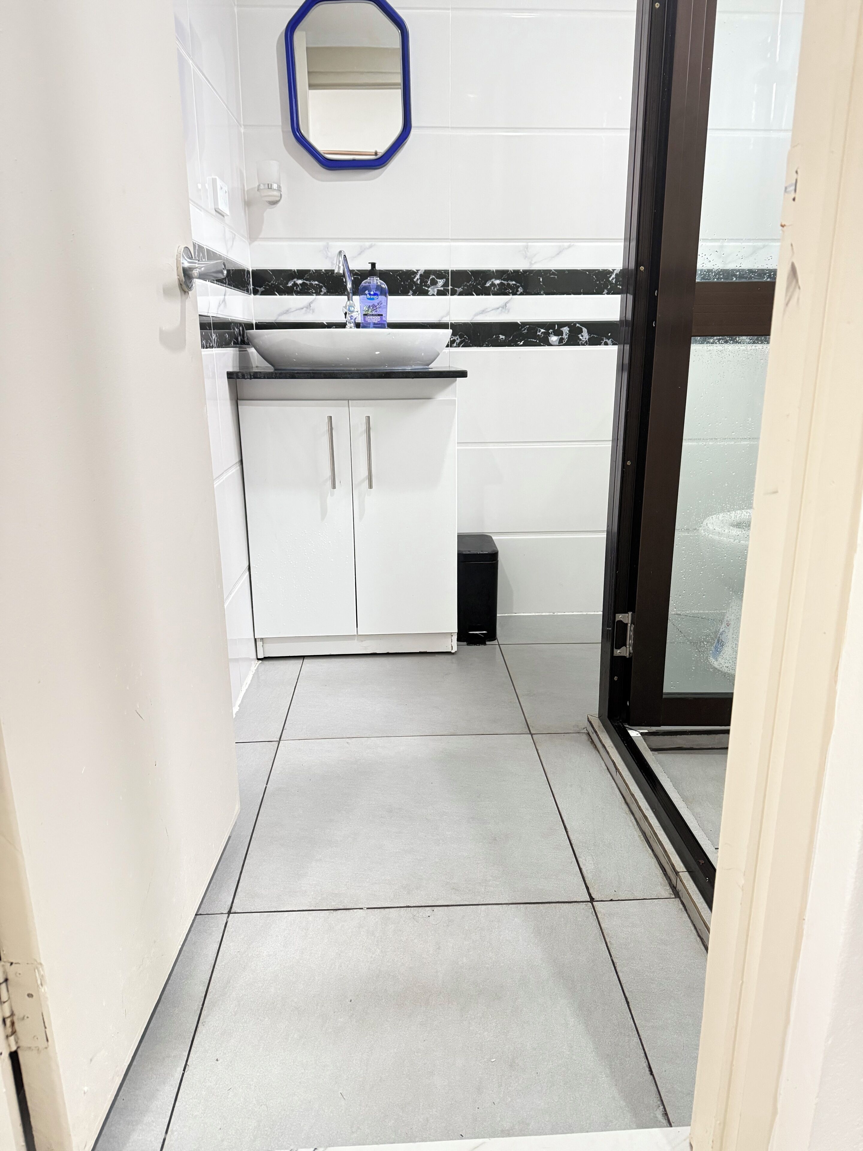 Un baño pequeño y moderno con un lavamanos blanco, salpicadero de mármol blanco y negro, y un espejo con marco azul.