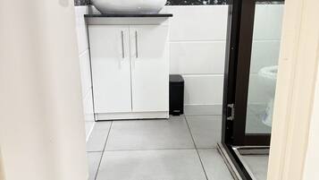 Un baño pequeño y moderno con un lavamanos blanco, salpicadero de mármol blanco y negro, y un espejo con marco azul.