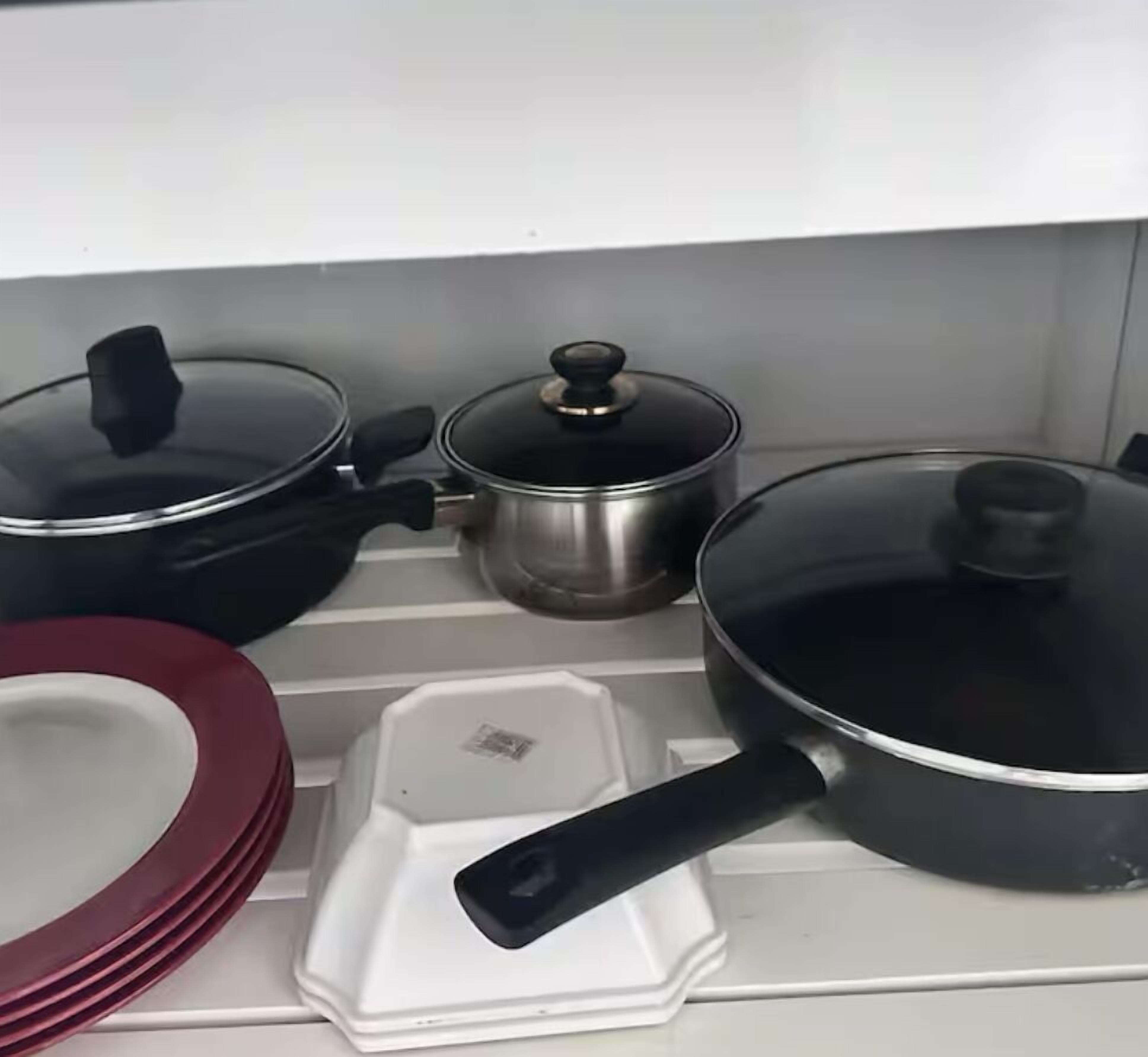 A kitchen shelf with various cookware including pots, pans, and a mixing bowl.