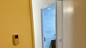 Un couloir avec une porte donnant sur une pièce dont un mur est en marbre et le sol en bois.
