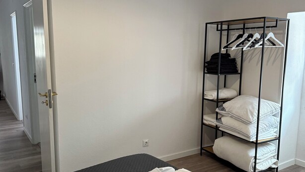 Une chambre à coucher comprenant un lit, un luminaire suspendu, une armoire avec des étagères et une porte donnant sur une autre pièce.