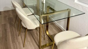 Un espace repas moderne avec une table à plateau en verre et des chaises blanches à revêtement tissu, dotées de pieds dorés.