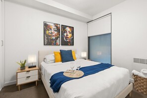 Habitació d'hotel moderna amb un llit gran, dues taules de nit, una petita planta en test i dos quadres abstractes a la paret.