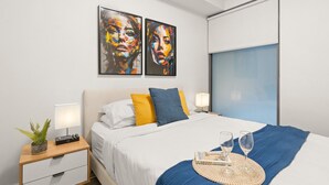 A modern bedroom with a bed, two bedside lamps, a bedside plant, and a window with a view.