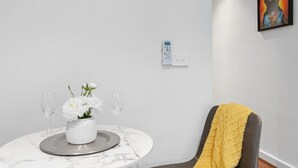 A modern room with a marble table, a white vase with flowers, two wine glasses, a chair with a yellow throw, and a painting on the wall.