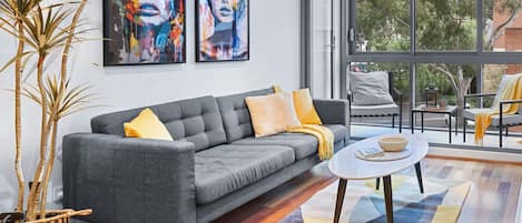 A modern living room with a grey sofa, yellow cushions, a round coffee table, and two large paintings on the wall.