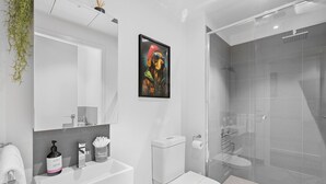 A modern bathroom with a white sink, toilet, and glass shower enclosure.