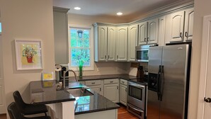 A modern kitchen with white cabinetry, stainless steel appliances, a central island, and a window with a view of greenery. - Convenient well appointed home near downtown Carrboro and farmers market (Carrboro)