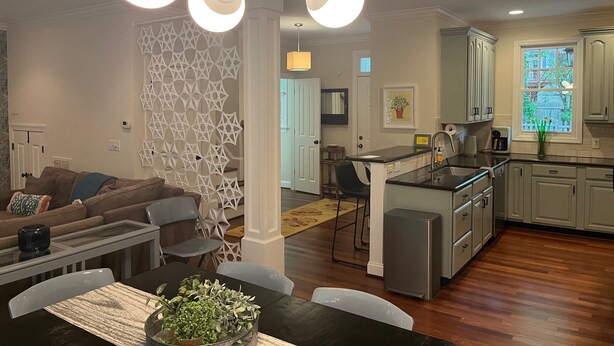 A modern kitchen with a central island, a dining area with a table and chairs, and a living room with a sofa and decorative wall panel. - Convenient well appointed home near downtown Carrboro and farmers market (Carrboro)