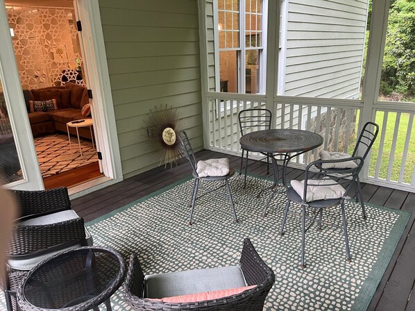 Un porche cubierto con mobiliario de mimbre, una mesa redonda y sillas.