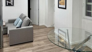 Een moderne woonkamer met een grijze bank, een glazen salontafel en een houten vloer.