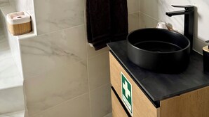 Een badkamer met een marmeren wand, een zwarte wastafel en een groen nooduitgangsbord.