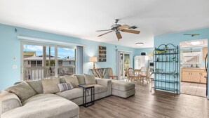 A spacious living room with a sectional sofa, a ceiling fan, and a view of the outside. - Walk To Beach, North End Restaurants, Night Life Steps Away! (Fort Myers Beach)