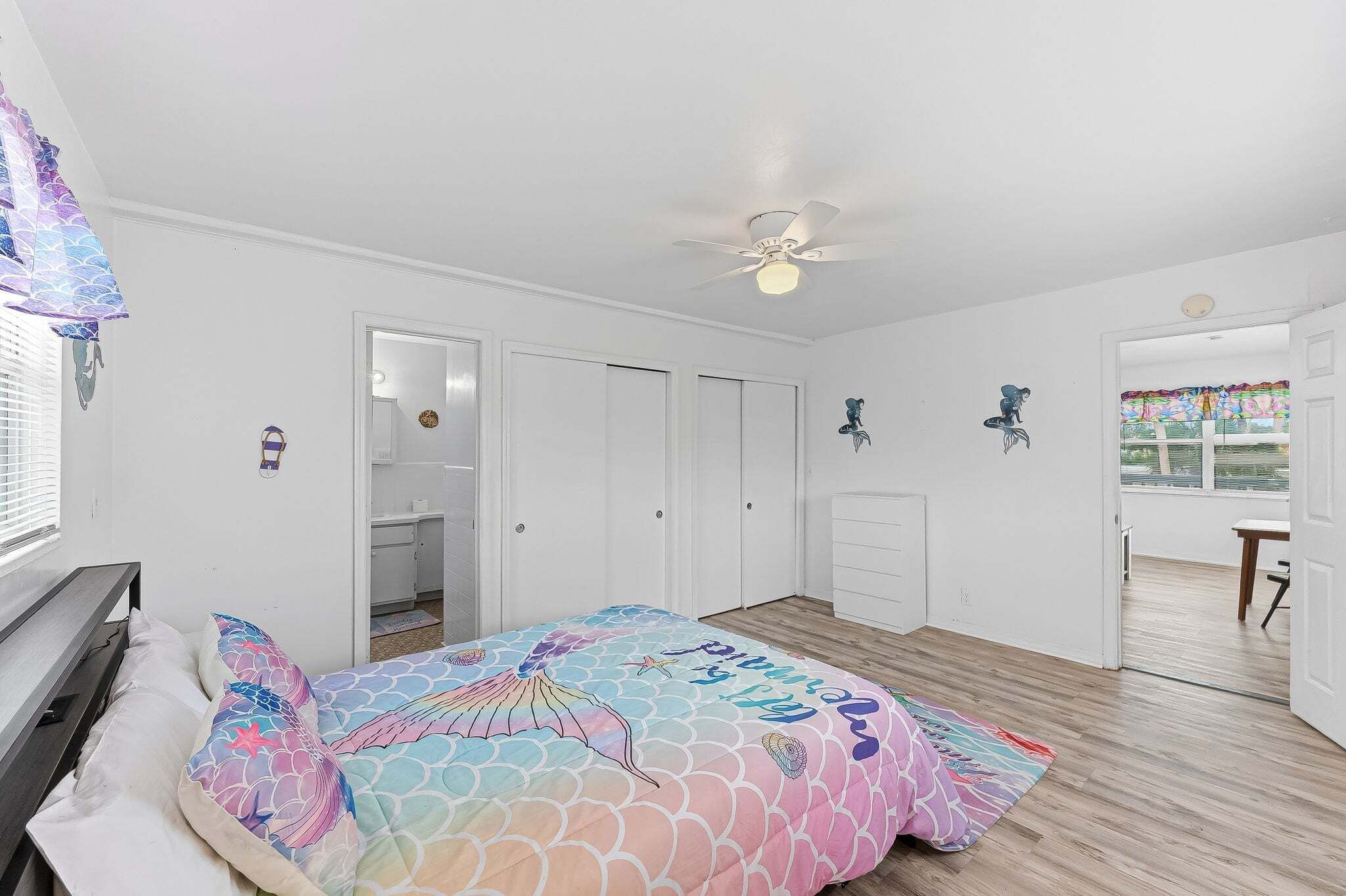 Una camera da letto con un letto, una ventola a soffitto, un armadio e una porta che dà su un'altra stanza.