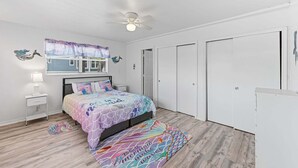 A bedroom with a bed, a ceiling fan, a window with curtains, a nightstand, and a wardrobe.