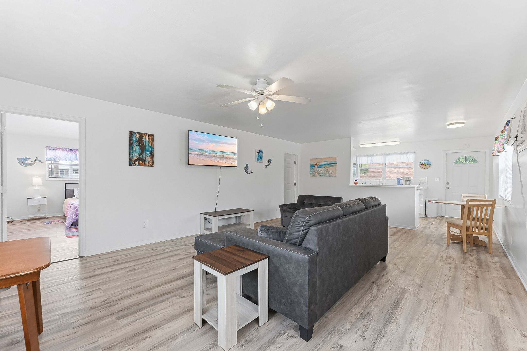 A spacious living area with a grey sofa, a wooden coffee table, a ceiling fan, and artwork on the walls.