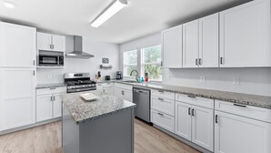 A modern kitchen with white cabinets, granite countertops, a built-in oven, and a stainless steel range hood. - Walk To Beach, North End Restaurants, Night Life Steps Away! (Fort Myers Beach)