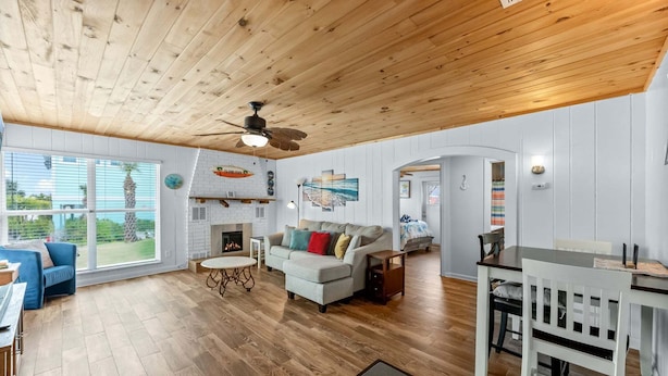 A spacious living room with a wooden ceiling, a fireplace, a sofa, a dining table with chairs, and large windows offering a view of the outdoors. - Walk To Beach, North End Restaurants, Night Life Steps Away! (Fort Myers Beach)