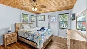 A bedroom with a wooden ceiling, a bed with a floral bedspread, a nightstand, and a dresser. - Walk To Beach, North End Restaurants, Night Life Steps Away! (Fort Myers Beach)