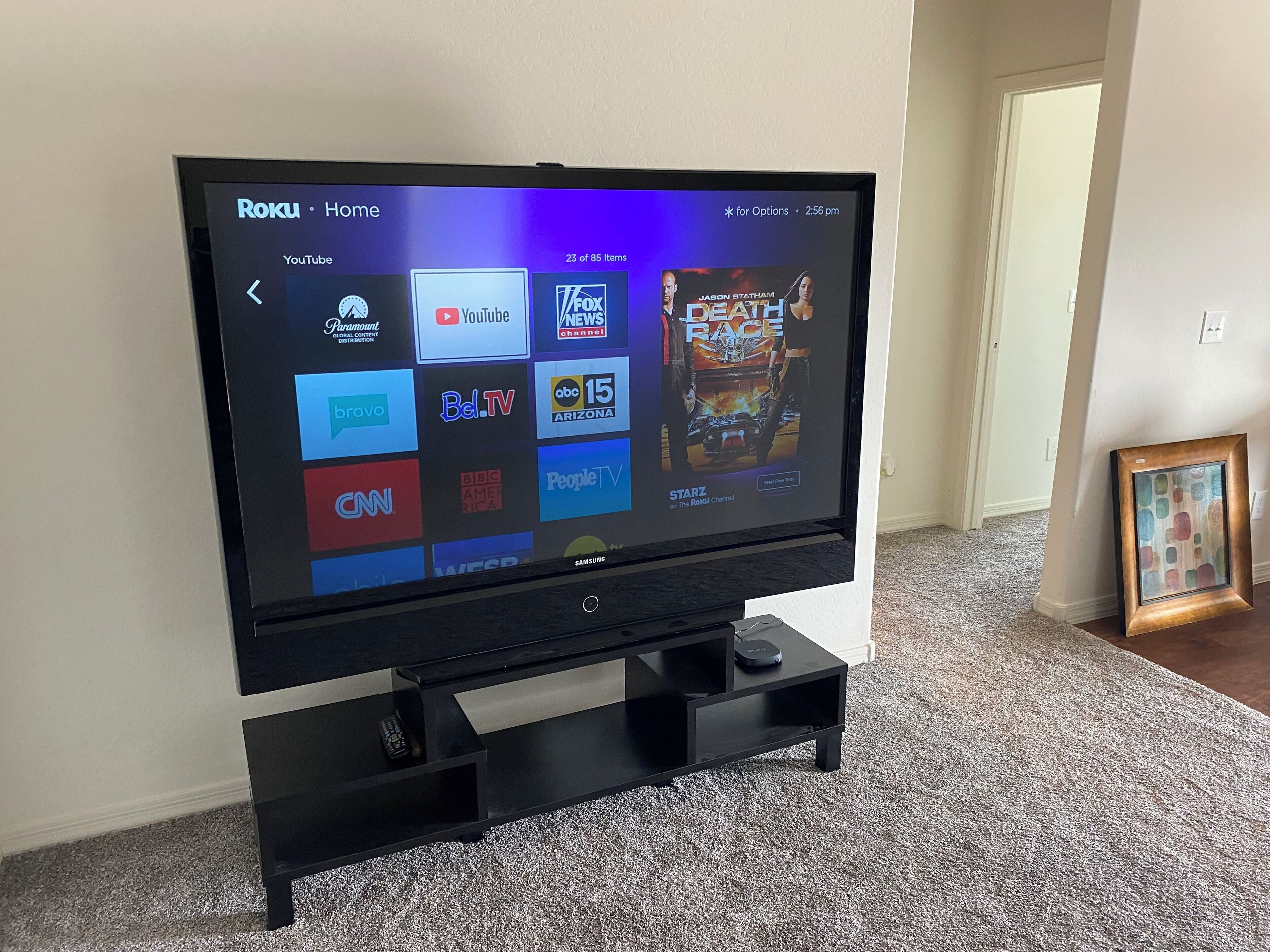 A flat-screen TV on a black stand displaying a Roku interface with various streaming service logos.