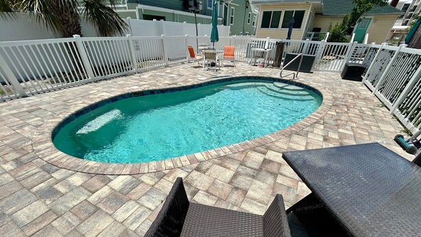 A swimming pool with a tiled deck, surrounded by white fences and outdoor furniture. - Walk To Beach, North End Restaurants, Night Life Steps Away! (Fort Myers Beach)