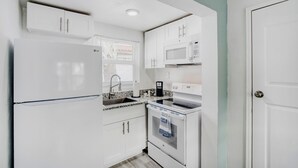 A compact kitchen with white cabinets, a microwave, an oven, and a sink. - 103 Studio in Melbourne (Melbourne)