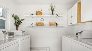 A laundry room with white cabinets, a washing machine, and shelves with baskets and a plant. - 103 Studio in Melbourne (Melbourne)